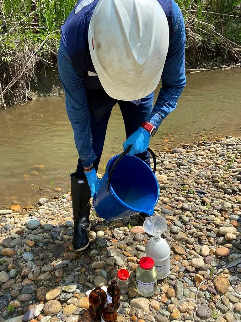 Toma de muestra de río con balde sobre un lecho de piedras