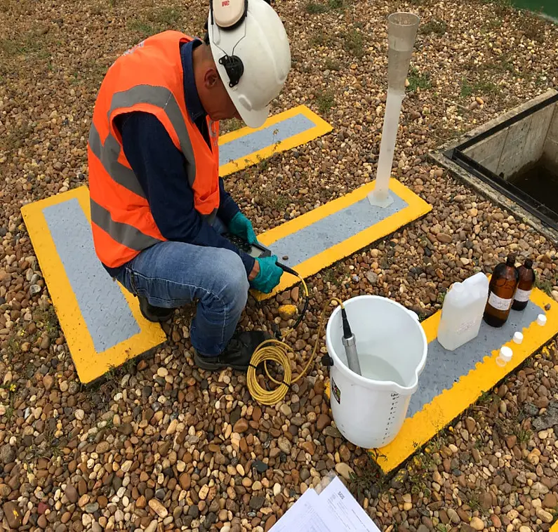 Técnico con chaleco mide sólidos sedimentables junto a un punto de vertimiento